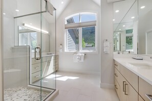 A modern bathroom with a glass shower enclosure, a large mirror, and a window providing a view of the outdoors. - Legends 10 4br 4ba 4 Bedroom Townhouse by RedAwning (Copper Mountain)