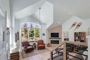 Un salón espacioso con un ventanal grande, una chimenea, sillones de cuero y una estantería.