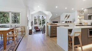 A modern kitchen with a large island, wooden chairs, and a view of trees through the windows. - Legends 10 4br 4ba 4 Bedroom Townhouse by RedAwning (Copper Mountain)