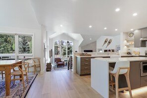 A modern kitchen with a large island, wooden chairs, and a view of trees through the windows. - Legends 10 4br 4ba 4 Bedroom Townhouse by RedAwning (Copper Mountain)