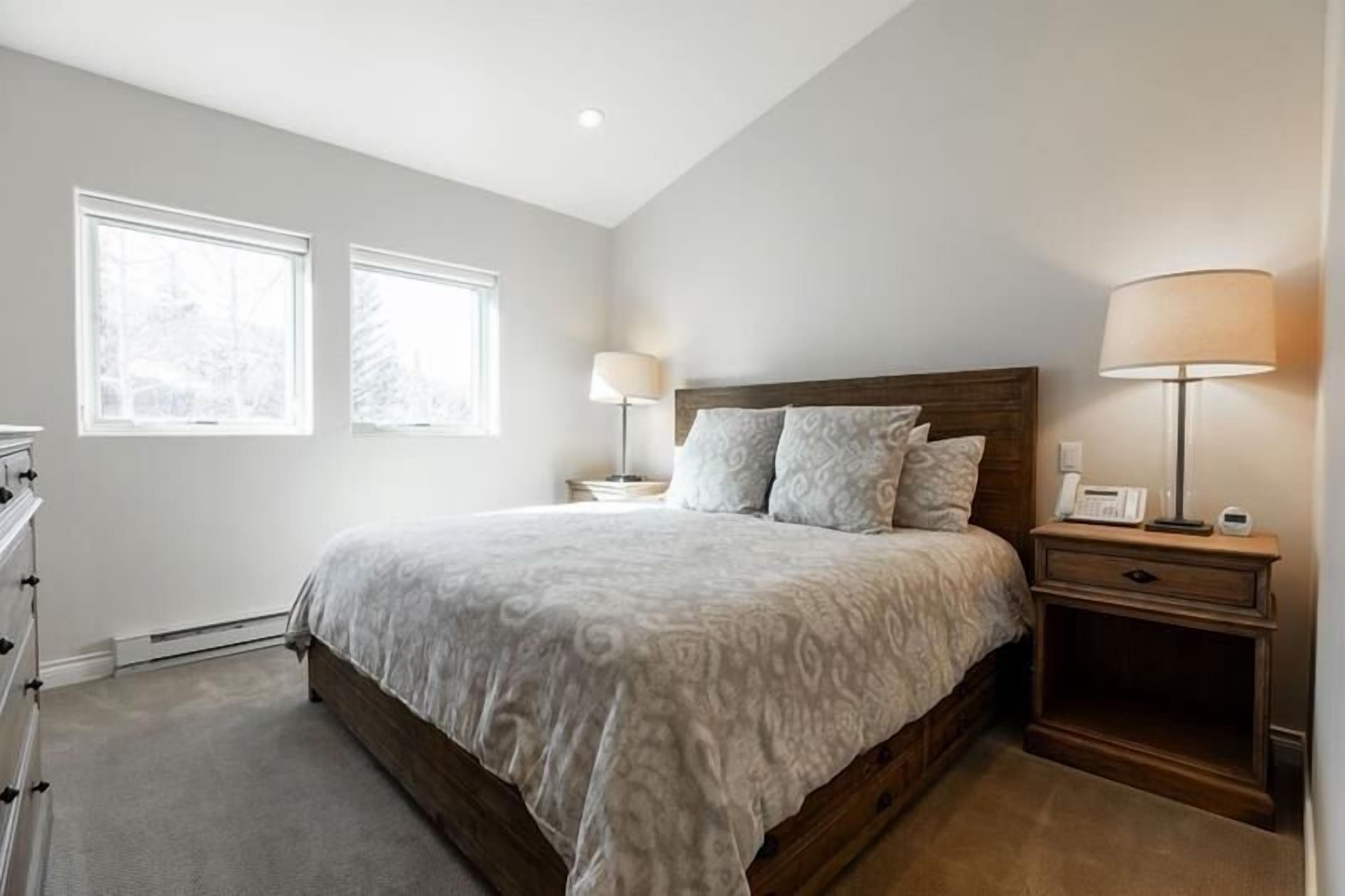 A bedroom with a large bed, two bedside lamps, a nightstand, and a dresser.