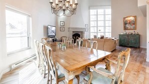 A spacious dining area with a large wooden table and chairs, a chandelier, and a fireplace.