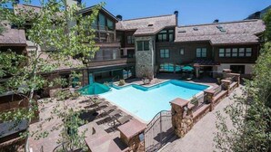 A multi-story building with a swimming pool, stone walls, and outdoor seating areas.
