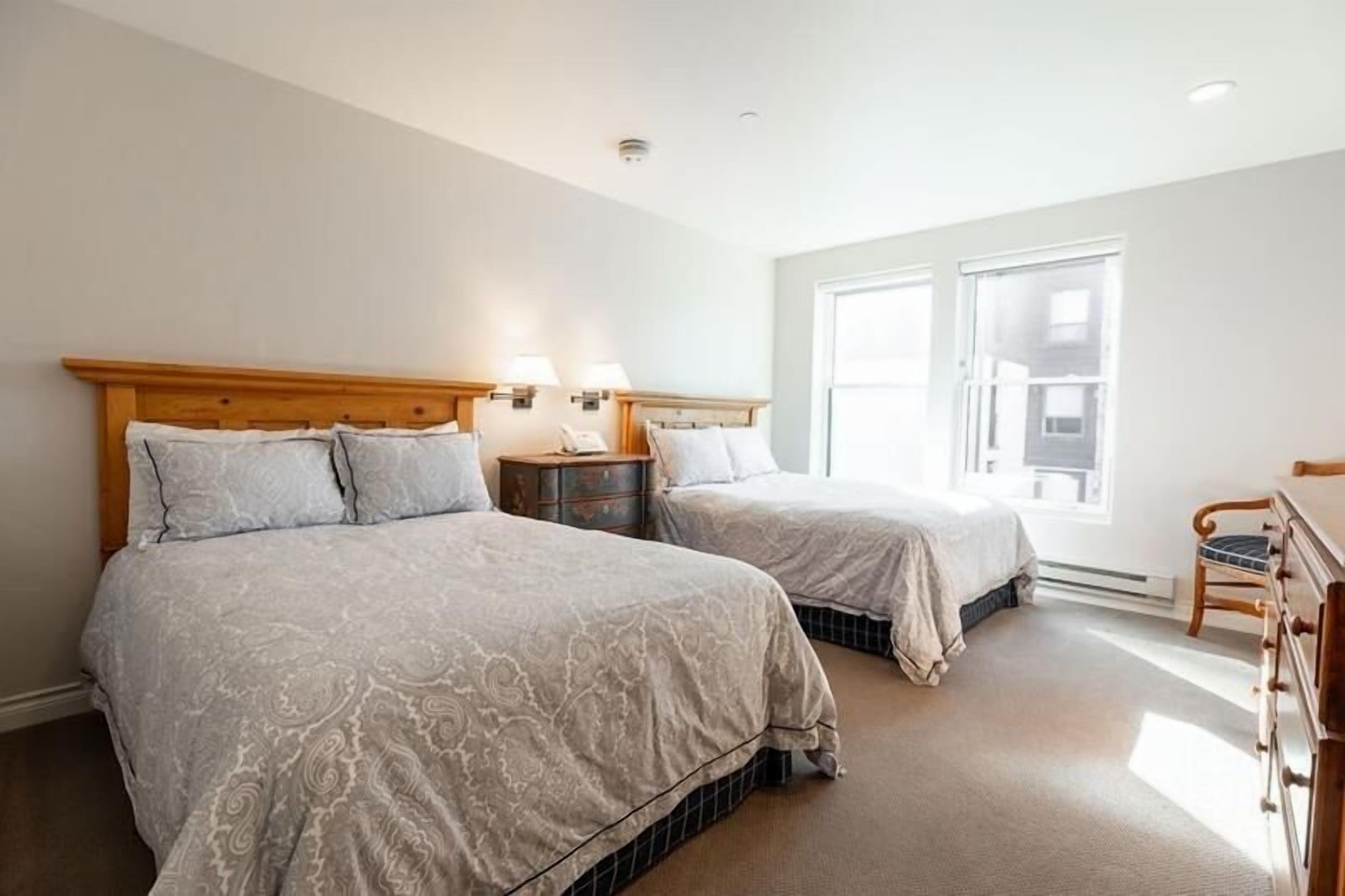 A hotel room with two beds, a wooden headboard, bedside lamps, a dresser, and a large window.