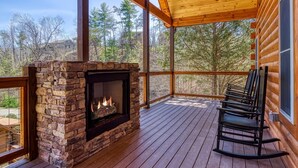 A stone fireplace on a wooden deck with a view of trees and a cabin in the background. - Er29 - Pop's Perch 2 Bedroom Cabin by RedAwning (Pigeon Forge)