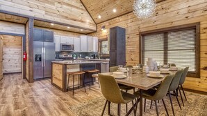 A modern kitchen with wooden walls and a dining area with a wooden table and chairs. - Er29 - Pop's Perch 2 Bedroom Cabin by RedAwning (Pigeon Forge)