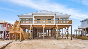 Ein zweistöckiges Strandhaus mit einer Holzterrasse und einer Treppe, die zum oberen Stock führt.