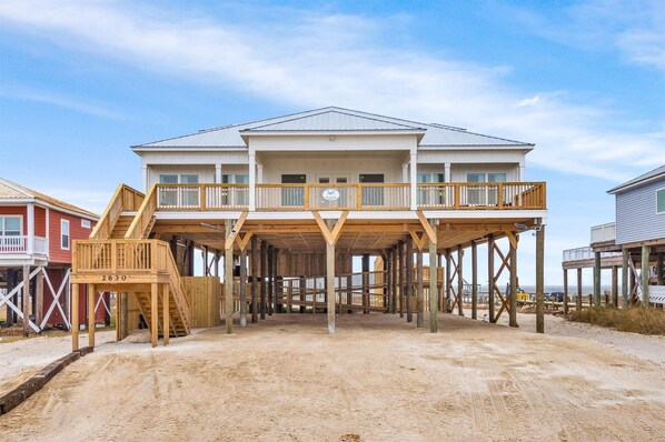 A two-story beachfront house with a wooden deck and a staircase leading to the upper level.
