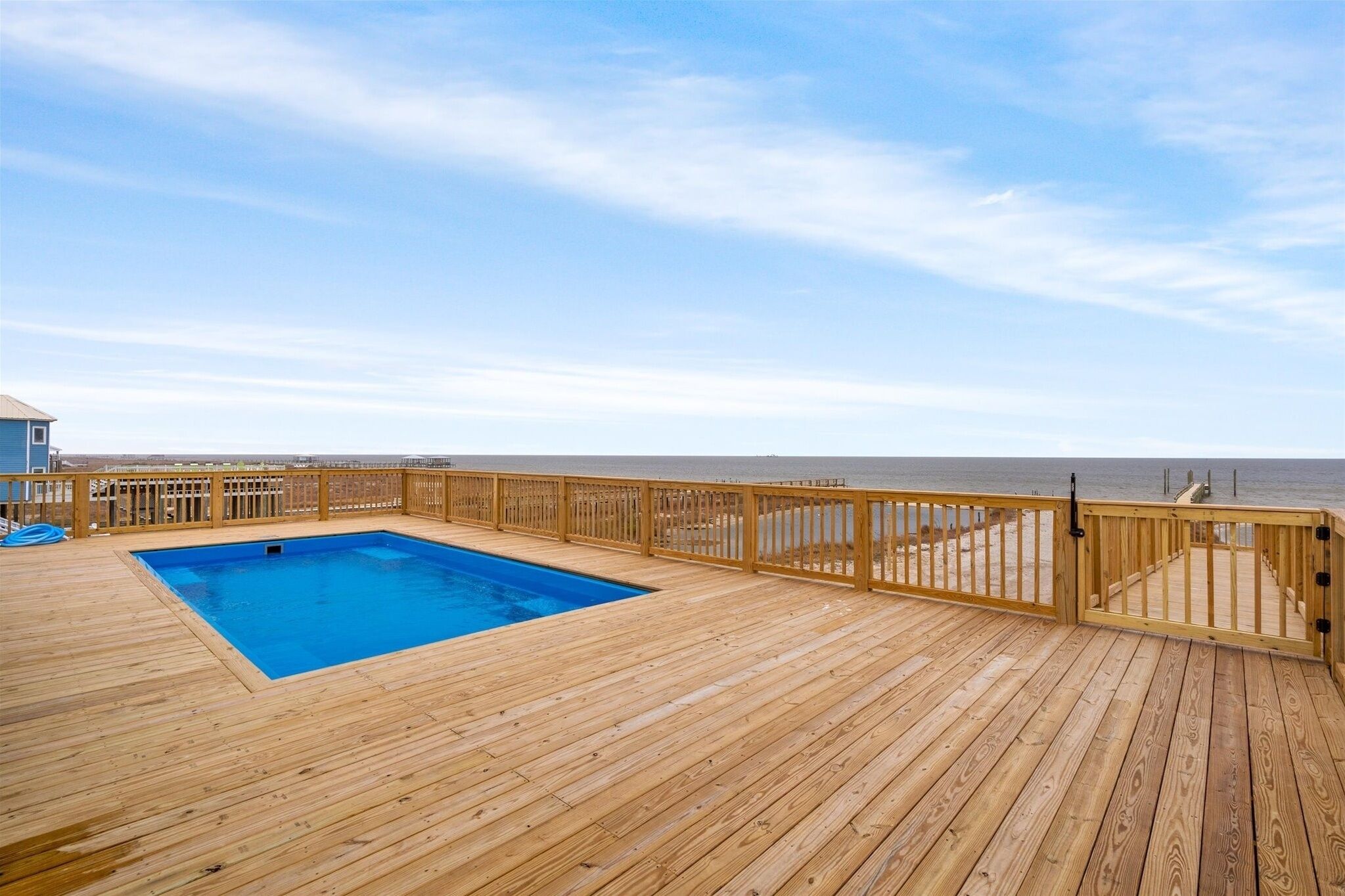 A wooden deck with a pool, wooden railings, and a view of the beach.