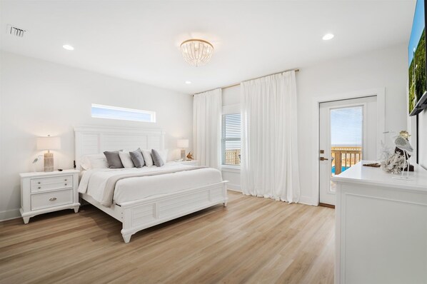 Un dormitorio con una cama grande, mesitas de noche blancas, un candelabro y vistas a un balcón.