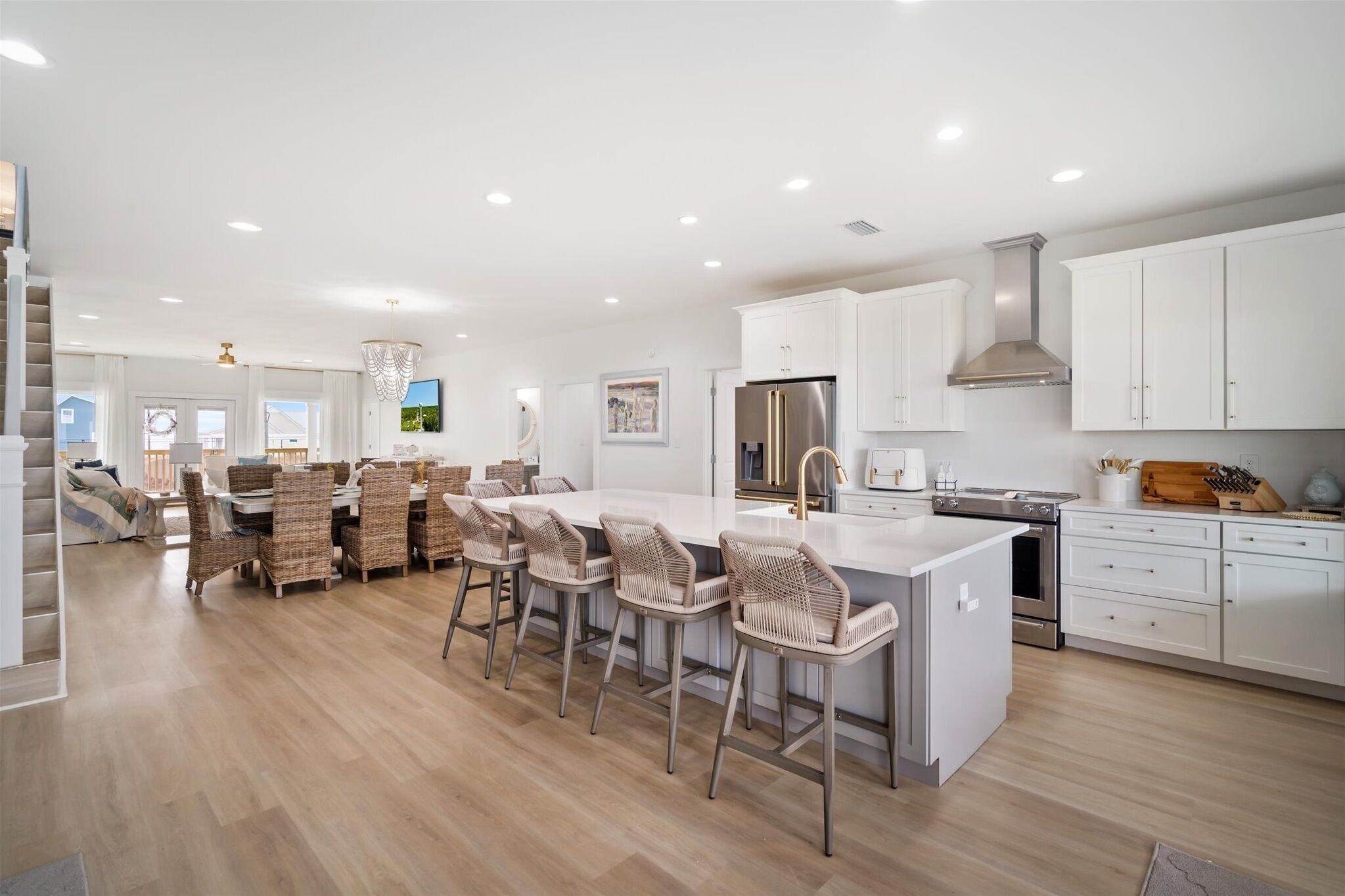 A modern kitchen with white cabinetry, a central island with bar stools, stainless steel appliances, and a staircase leading to another level.