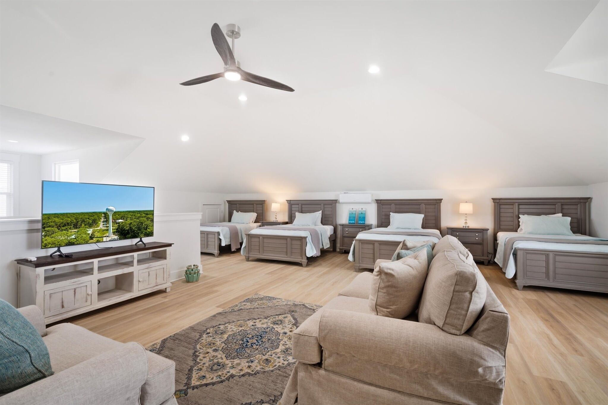 A modern, well-lit room with a ceiling fan, a flat-screen TV, a sofa, and a bed with a headboard.