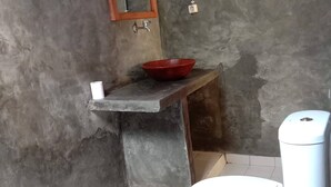 Ein Badezimmer mit einer weißen Toilette, einem roten Waschbecken auf einer Steinarbeitsplatte, einem spiegelnden Wandbild mit Holzrahmen und einem gefliesten Boden.