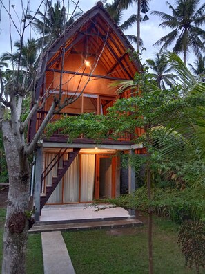 A two-story wooden house with a balcony, surrounded by lush greenery and palm trees. - Jungle House - surf & stay (Mendoyo)