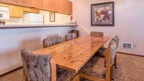 A dining area with a wooden table and patterned chairs, a kitchen with wooden cabinets, and a framed picture on the wall.