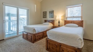 A bedroom with two wooden beds, a sliding glass door, and a window with blinds.