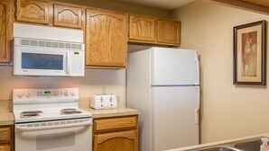 A compact kitchen with wooden cabinets, a microwave, a stove, a toaster, and a refrigerator.