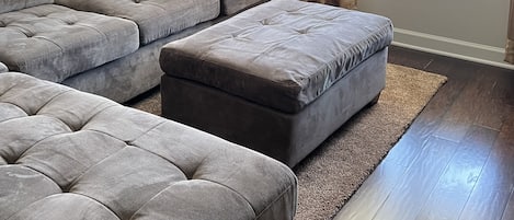 A living room with a sectional sofa, ottoman, and a chandelier.