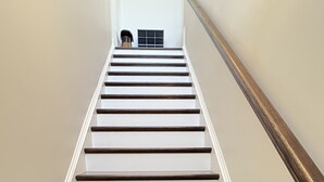 Un escalier dont les marches alternent entre le blanc et le bois foncé, avec des murs blancs et une main courante en bois.