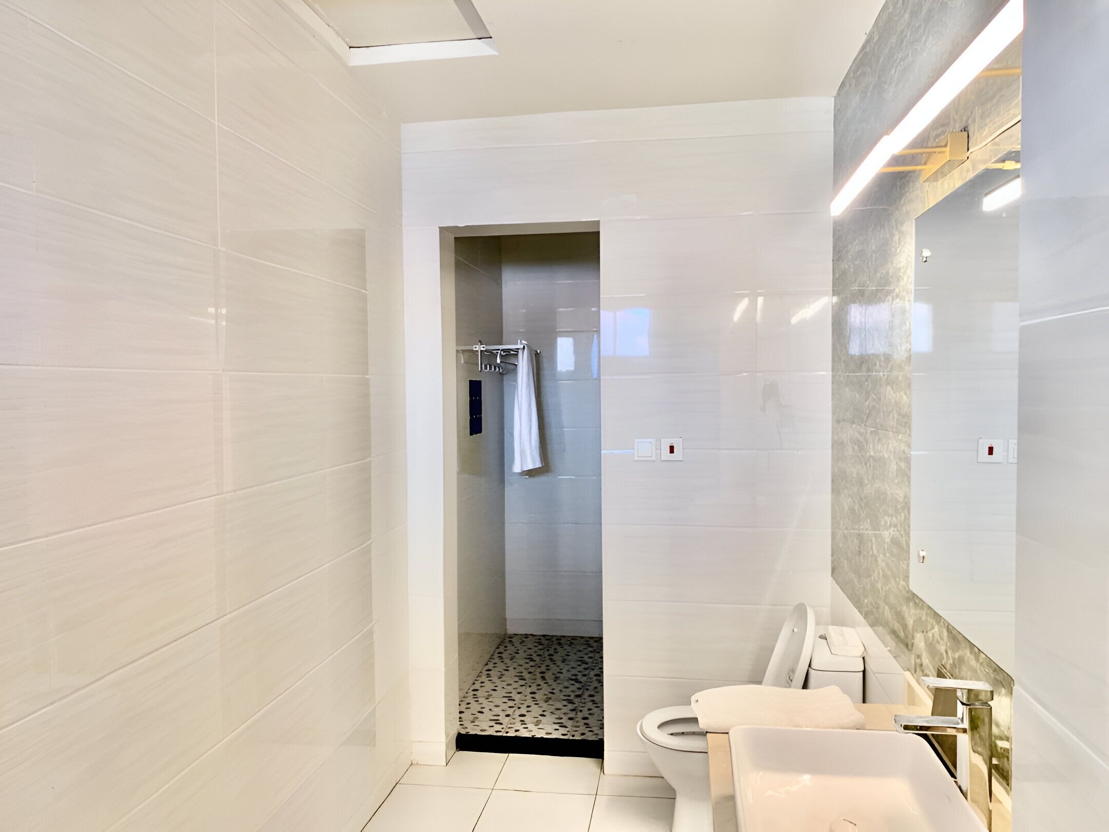 A modern bathroom with white tiles, a shower area, a toilet, and a sink.