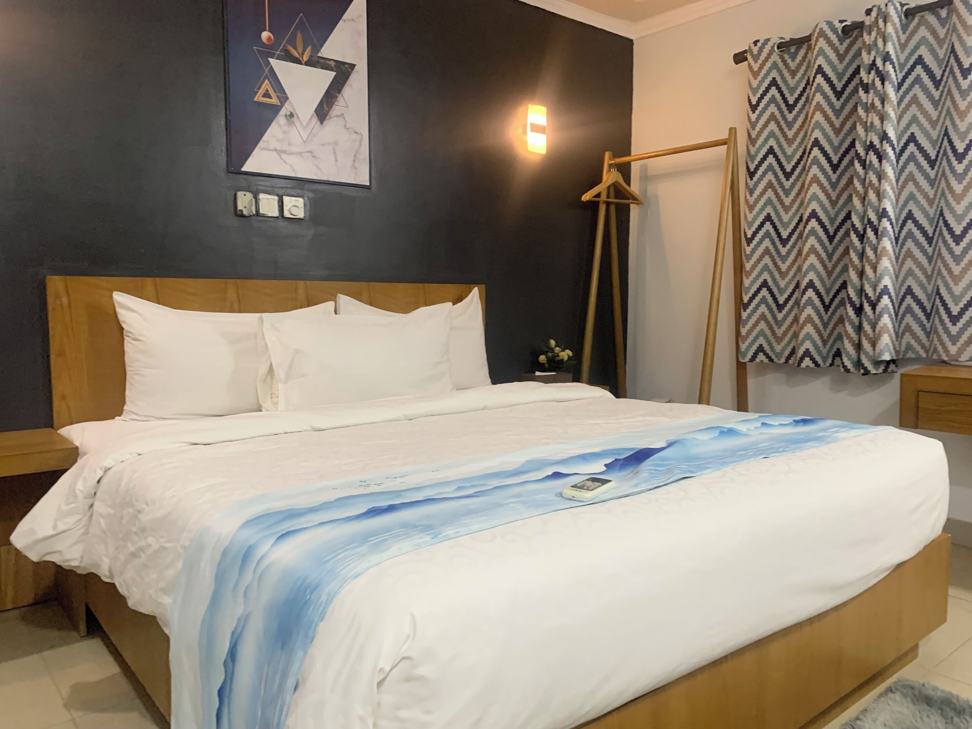 Een netjes opgemaakt bed met witte lakens en een blauw-wit abstract ontwerp op de deken.