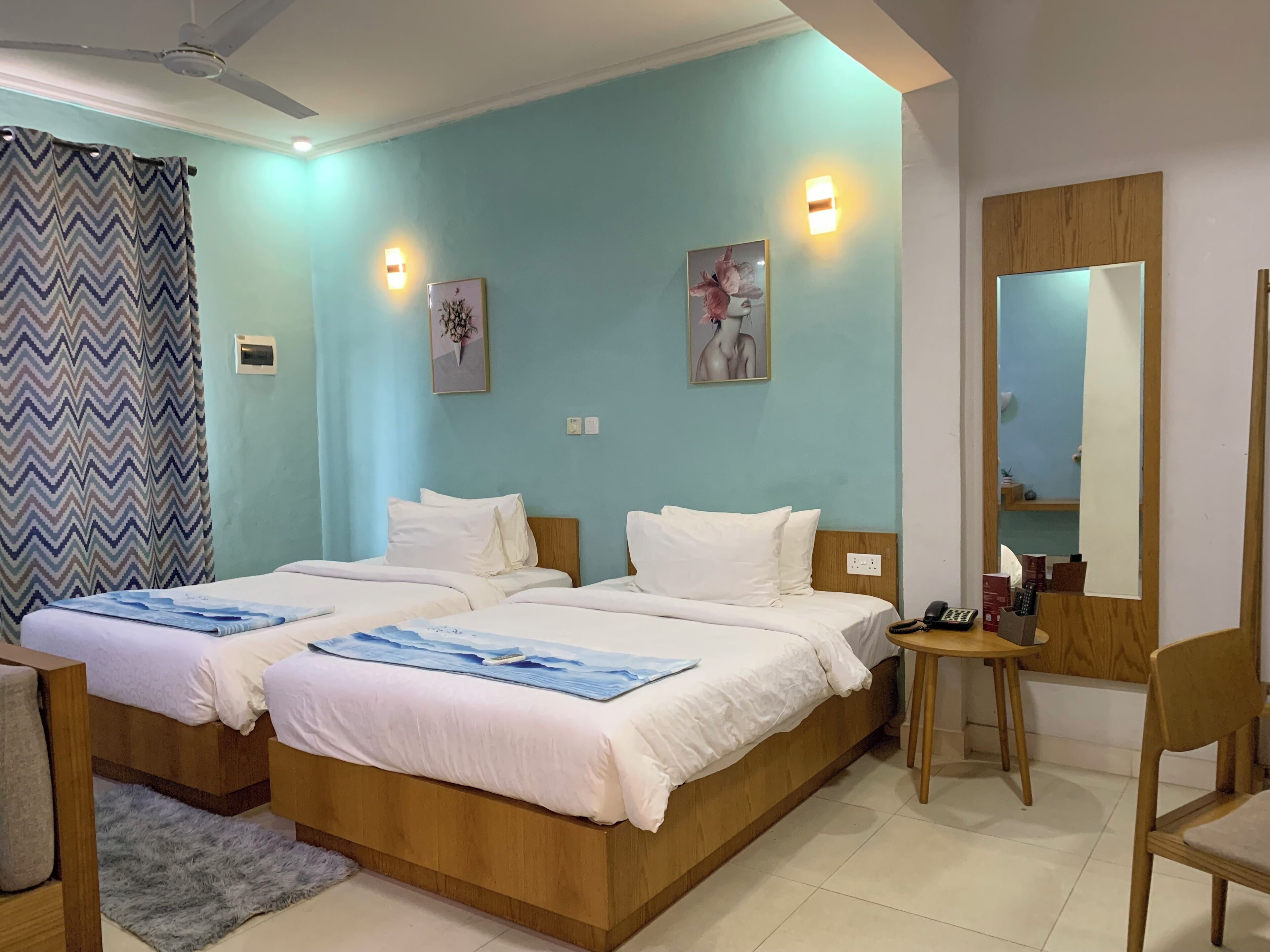 A hotel room with two beds, a desk, a chair, a mirror, and artwork on the walls.