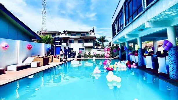 A swimming pool with a clear blue sky, a tall communication tower, and a building with large windows. - Canwin Hotel (Accra)