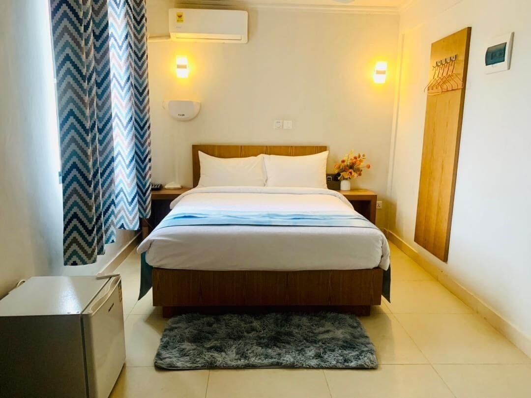 Une chambre d’hôtel comprenant un lit, une table de chevet, une lampe, un radiateur, une armoire et un tapis.