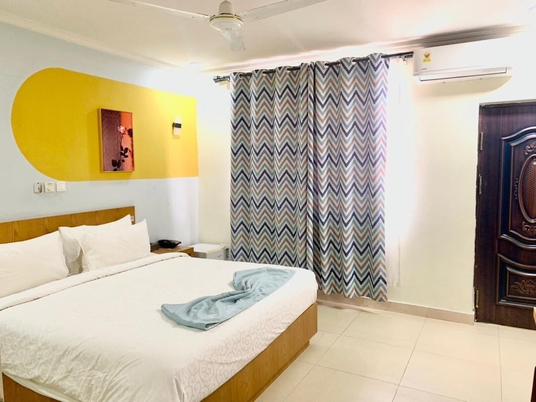 Ein Hotelzimmer mit einem Bett, einem Nachttisch, einer Wandklimaanlage und einer Tür mit dekorativer Verkleidung.