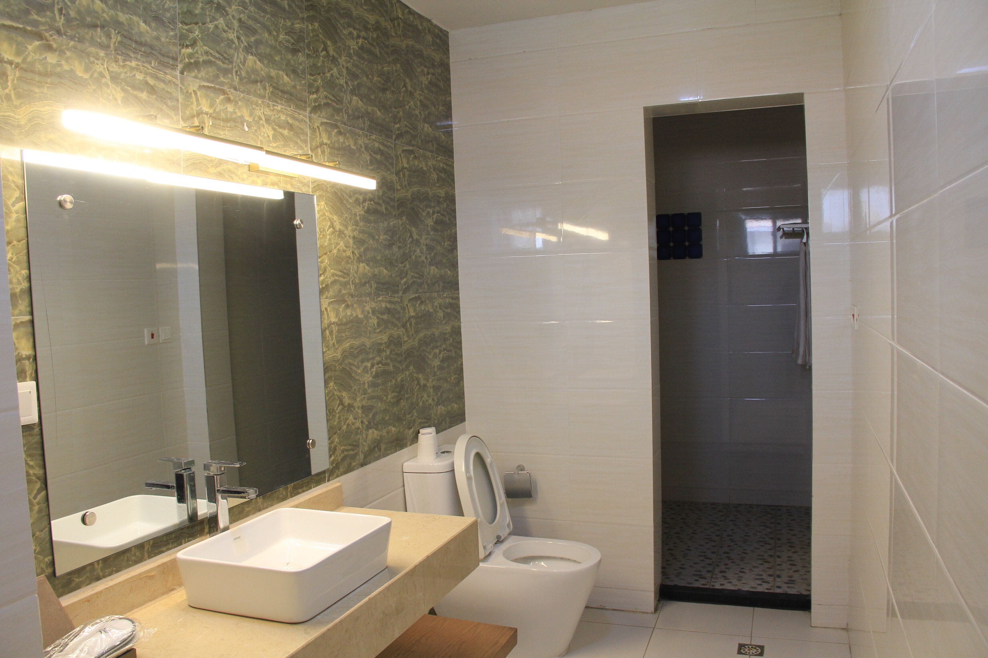 A modern bathroom with a large mirror, a rectangular sink, a toilet, and a shower area.
