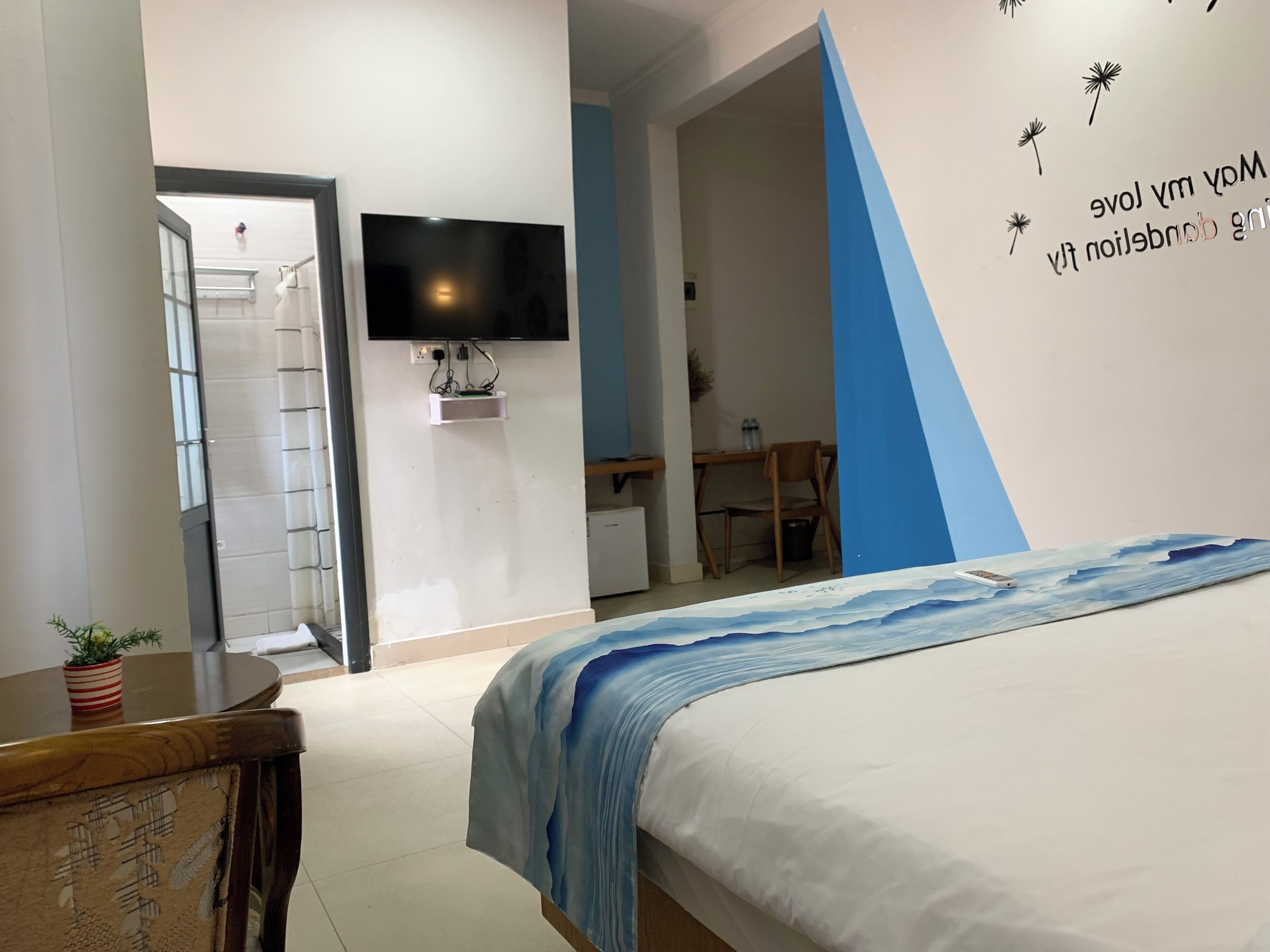 Un dormitorio con cama, escritorio, silla, televisor montado en la pared y puerta que da a otra habitación.