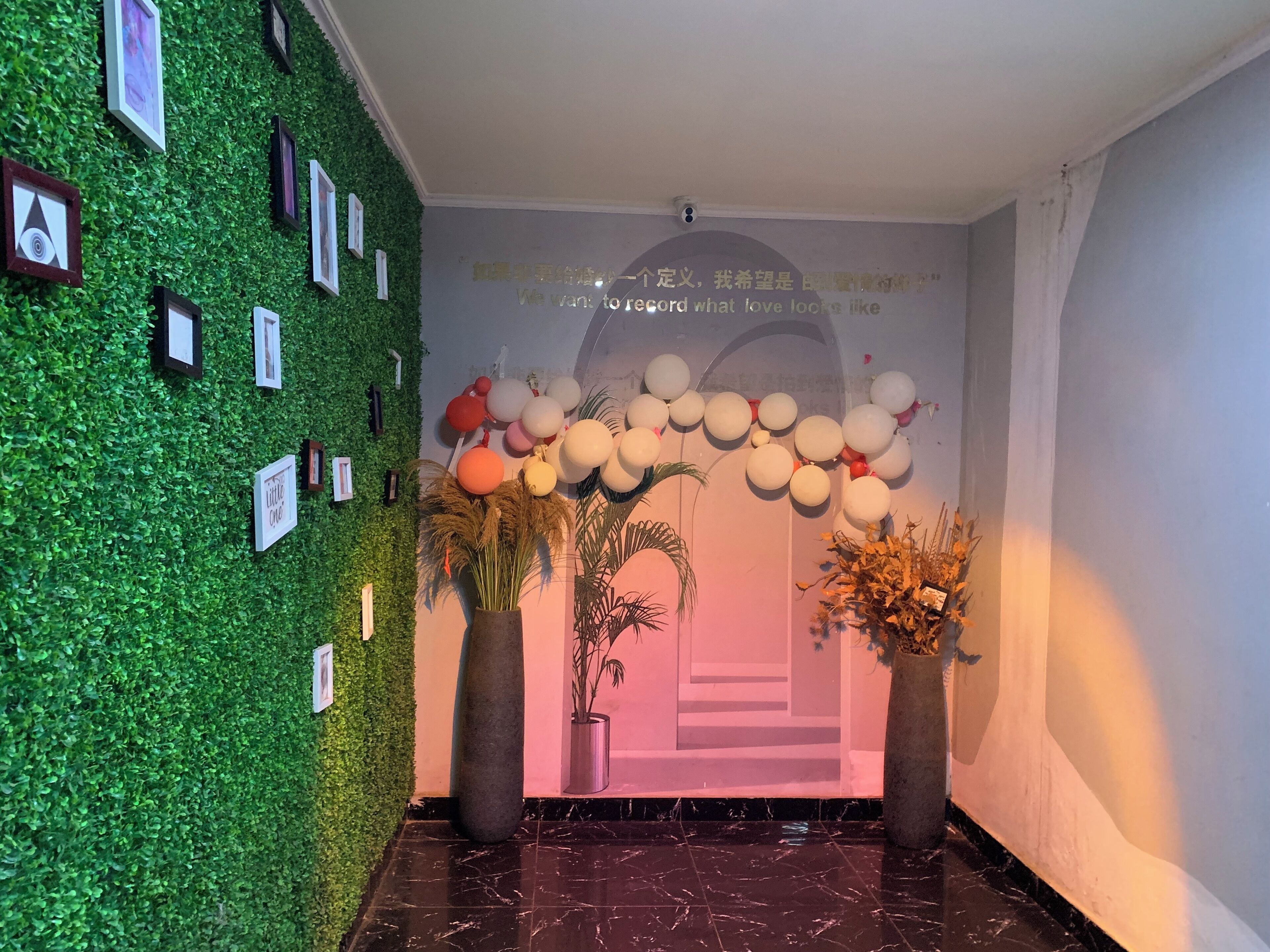 A lobby with a green wall adorned with framed pictures, a marble floor, and a wall with a decorative archway and balloons.