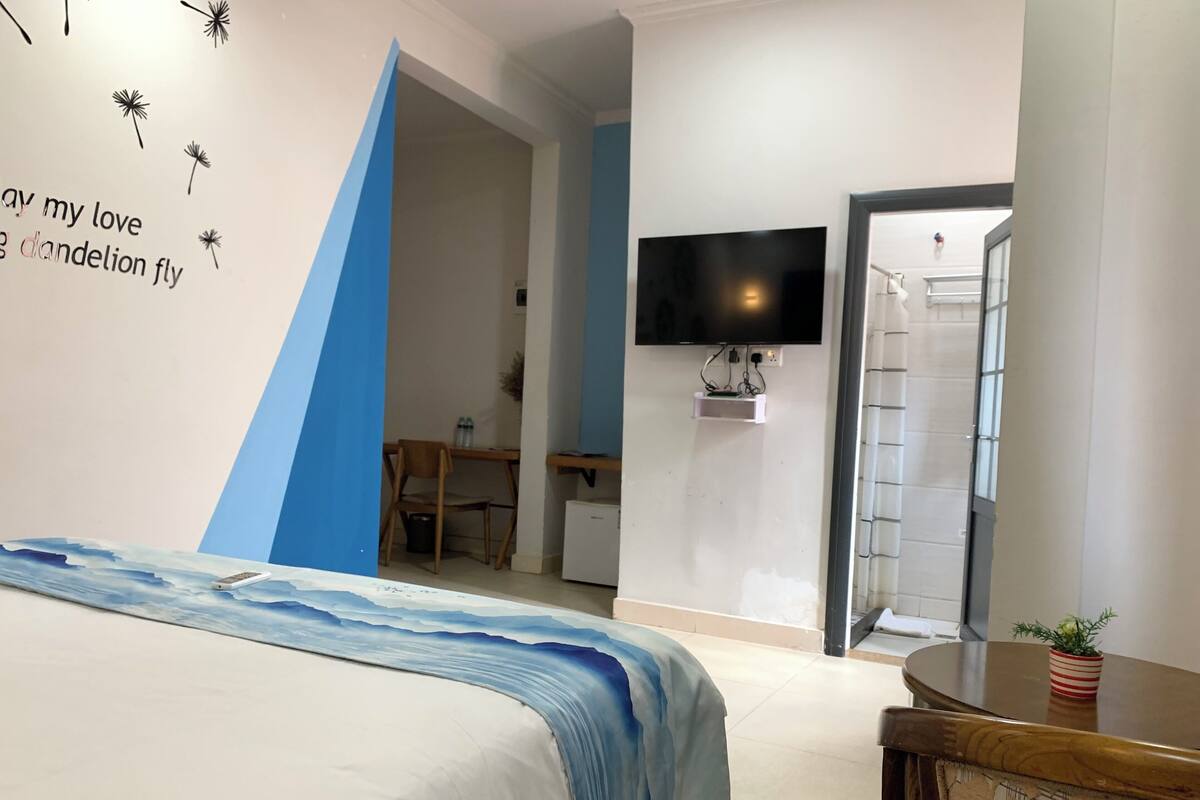 A hotel room with a bed, a desk, a television mounted on the wall, and a door leading to another room.