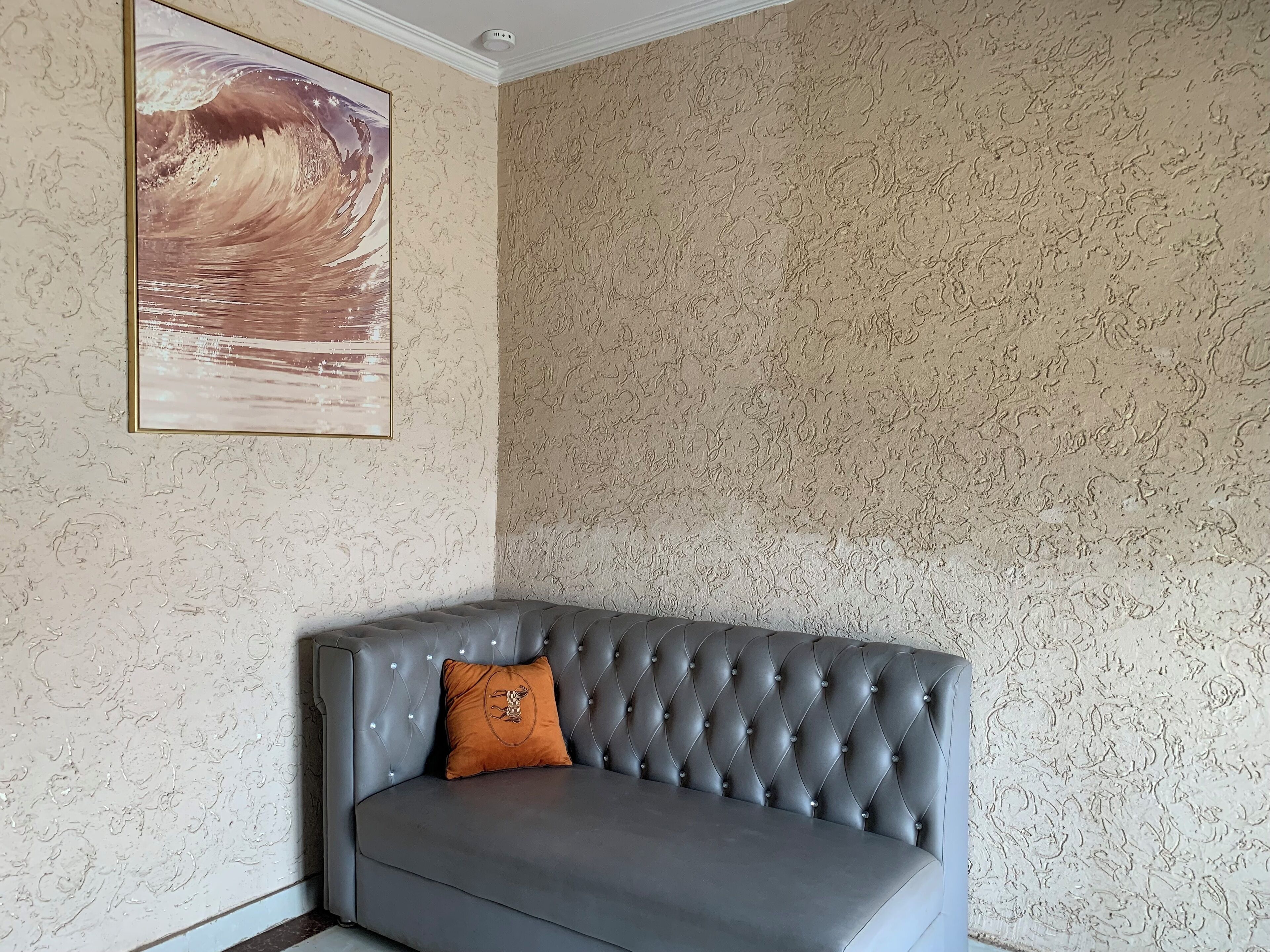 Quarto nos fundos com um sofá cinza estofado, parede com textura e uma obra de arte emoldurada.