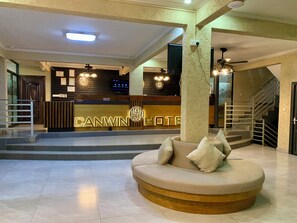 Un hall de hotel con mostrador de recepción, una escalera y una zona de estar circular.