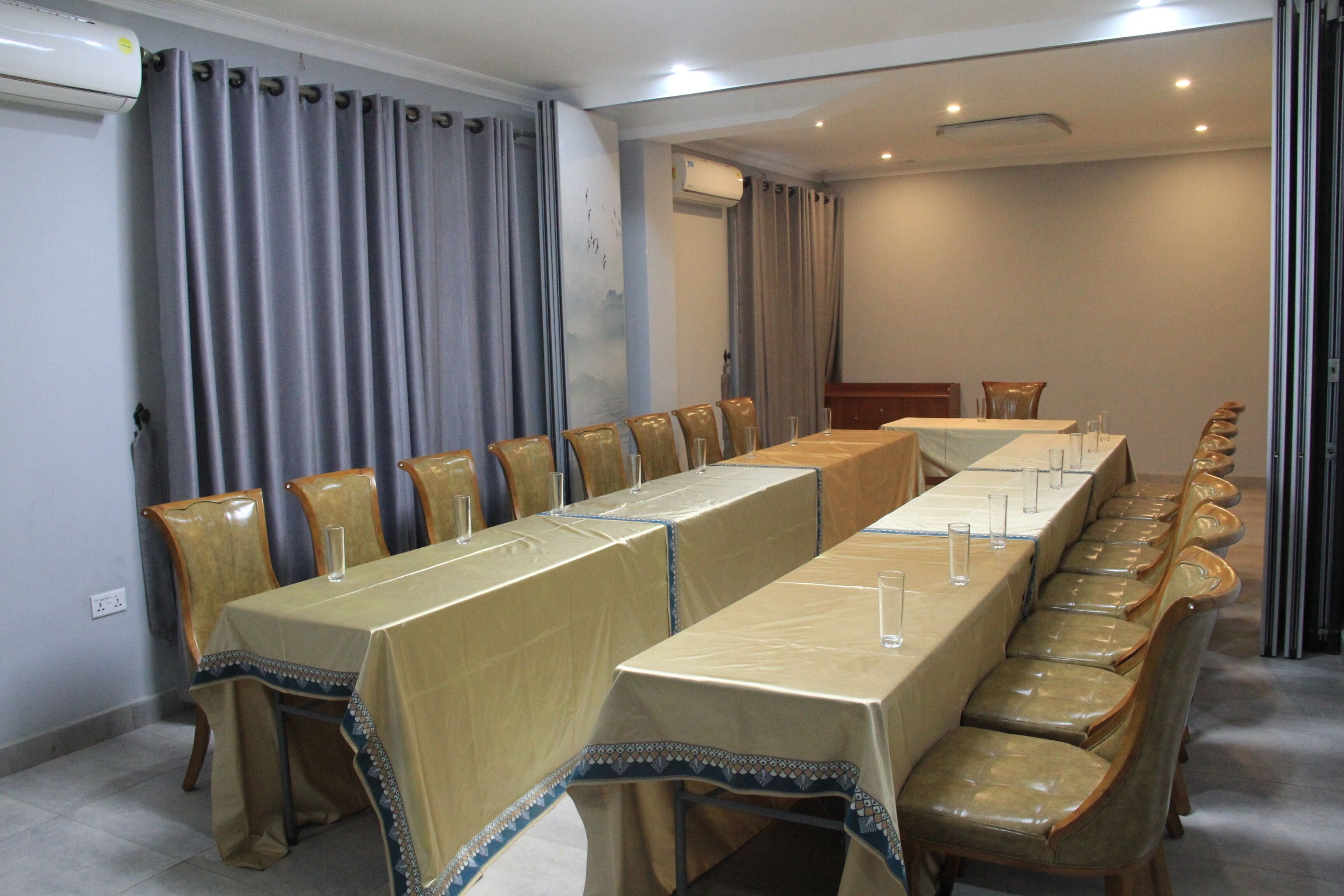 Une salle de conférence équipée d’une longue table et de chaises, de climatiseurs et de rideaux.
