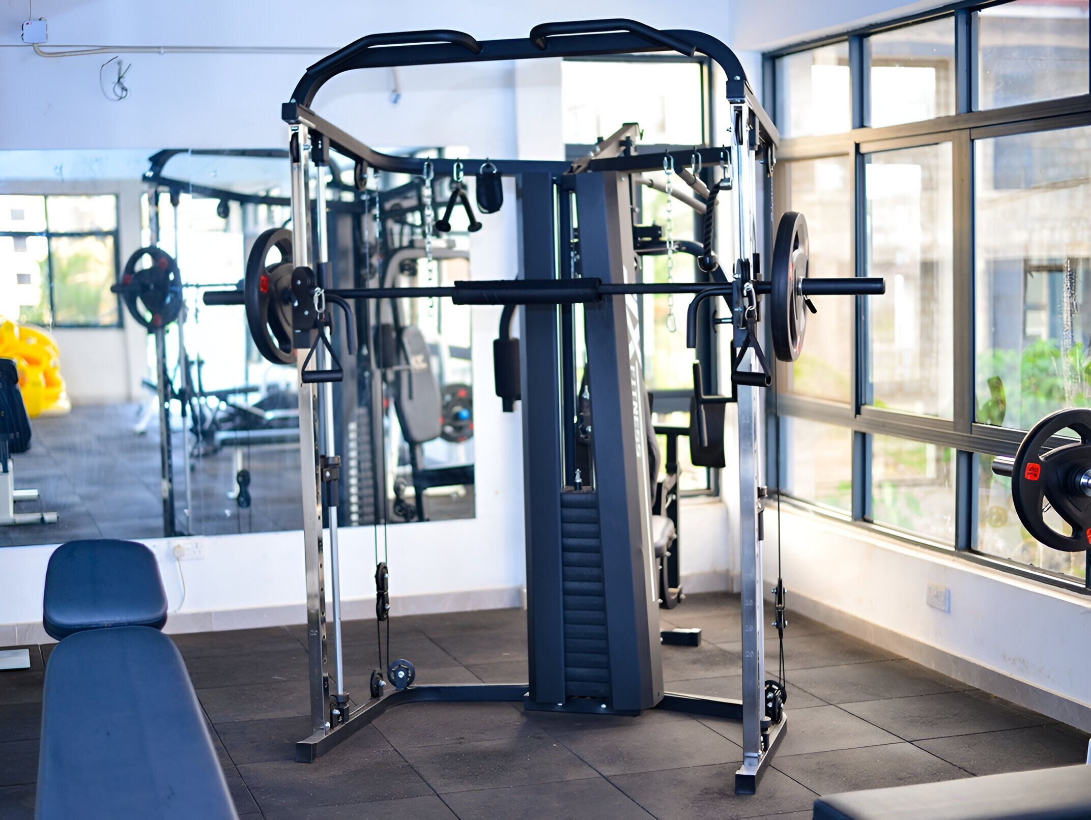 A gym with a weightlifting station, benches, and large windows.