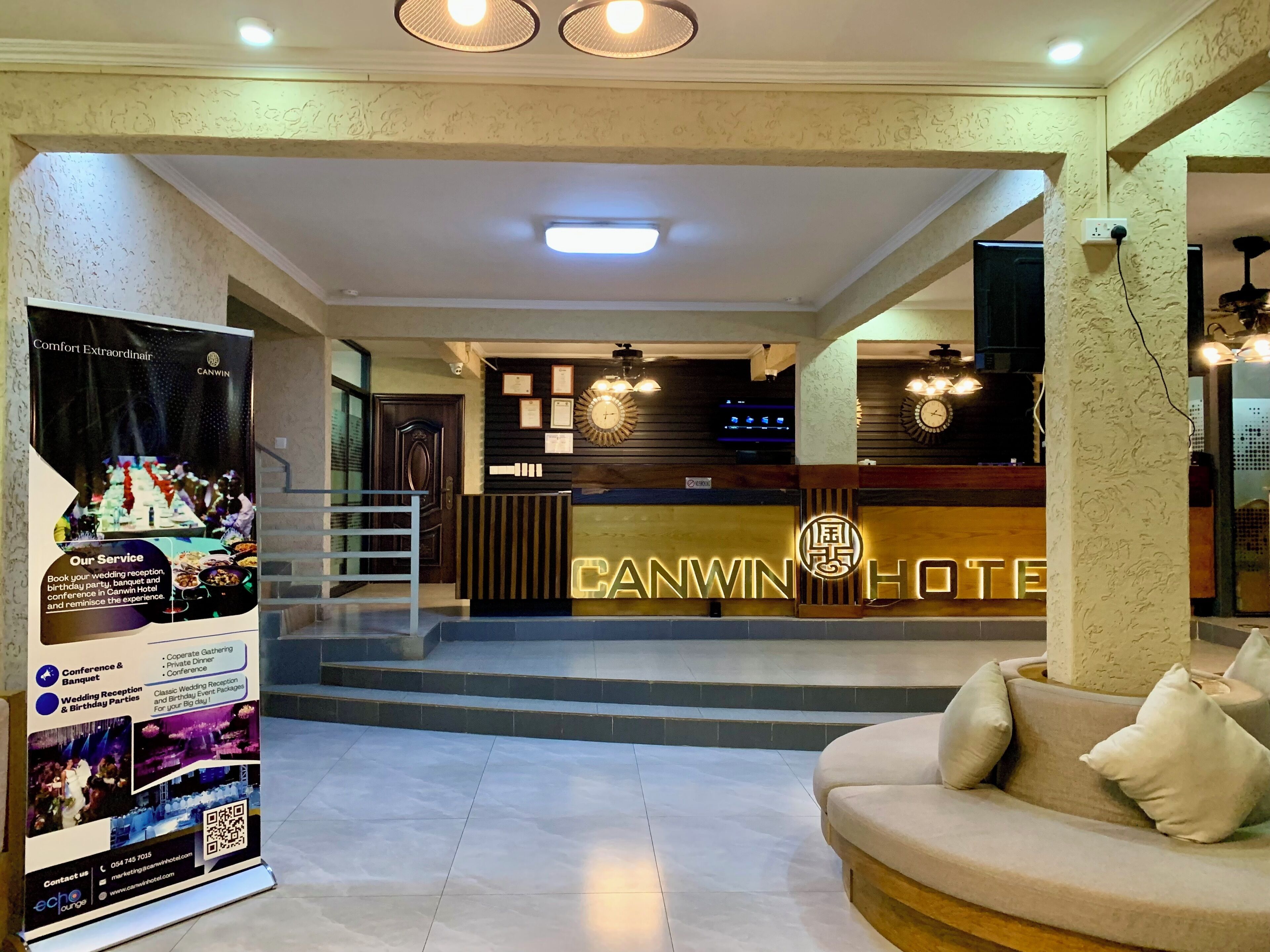 Uma área de recepção de hotel com design moderno, incluindo um balcão de atendimento, uma escadaria e uma sala de estar com um sofá.