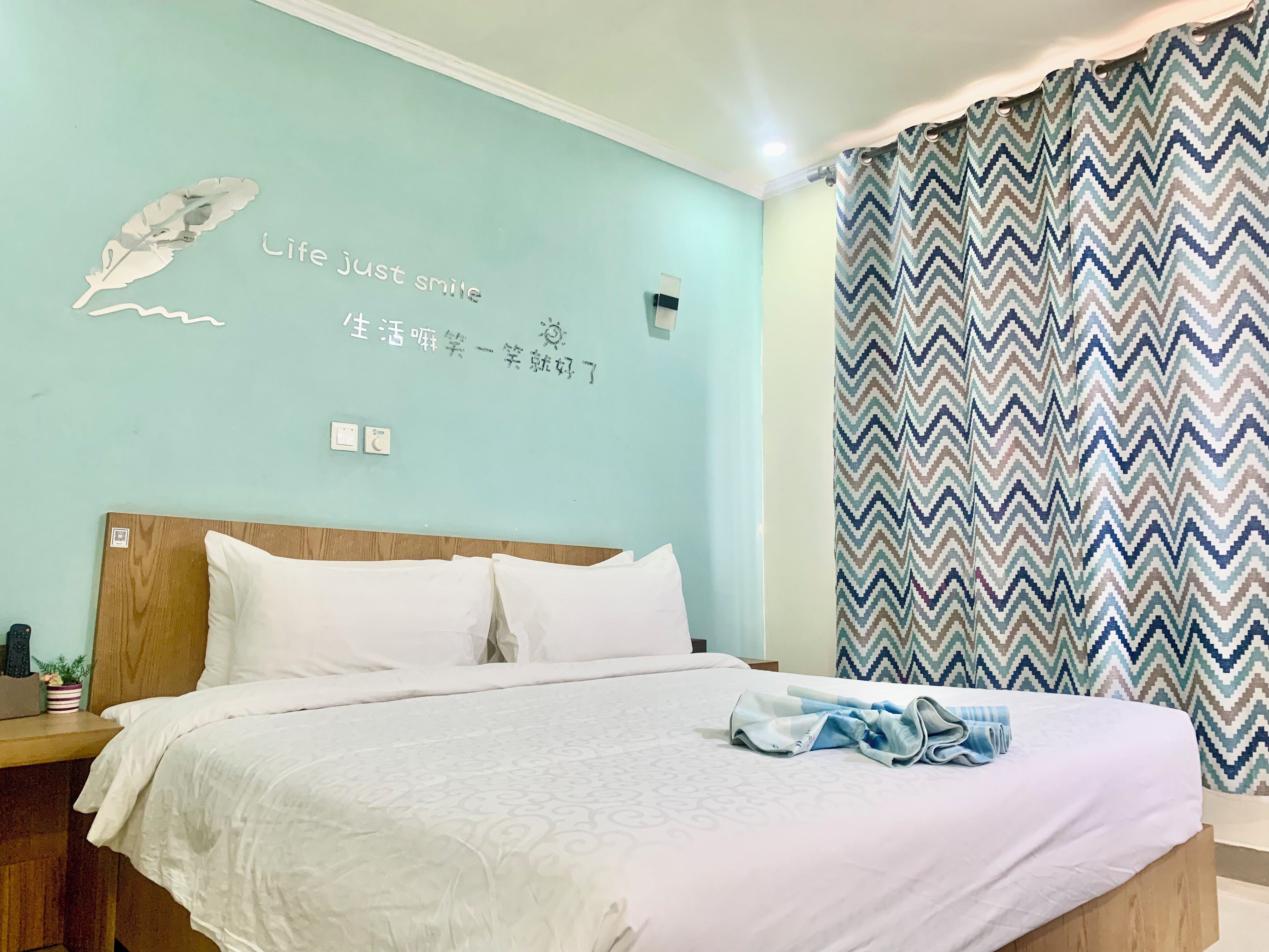A neatly made bed with white bedding, a wooden headboard, and a wall with motivational text and a decorative feather.