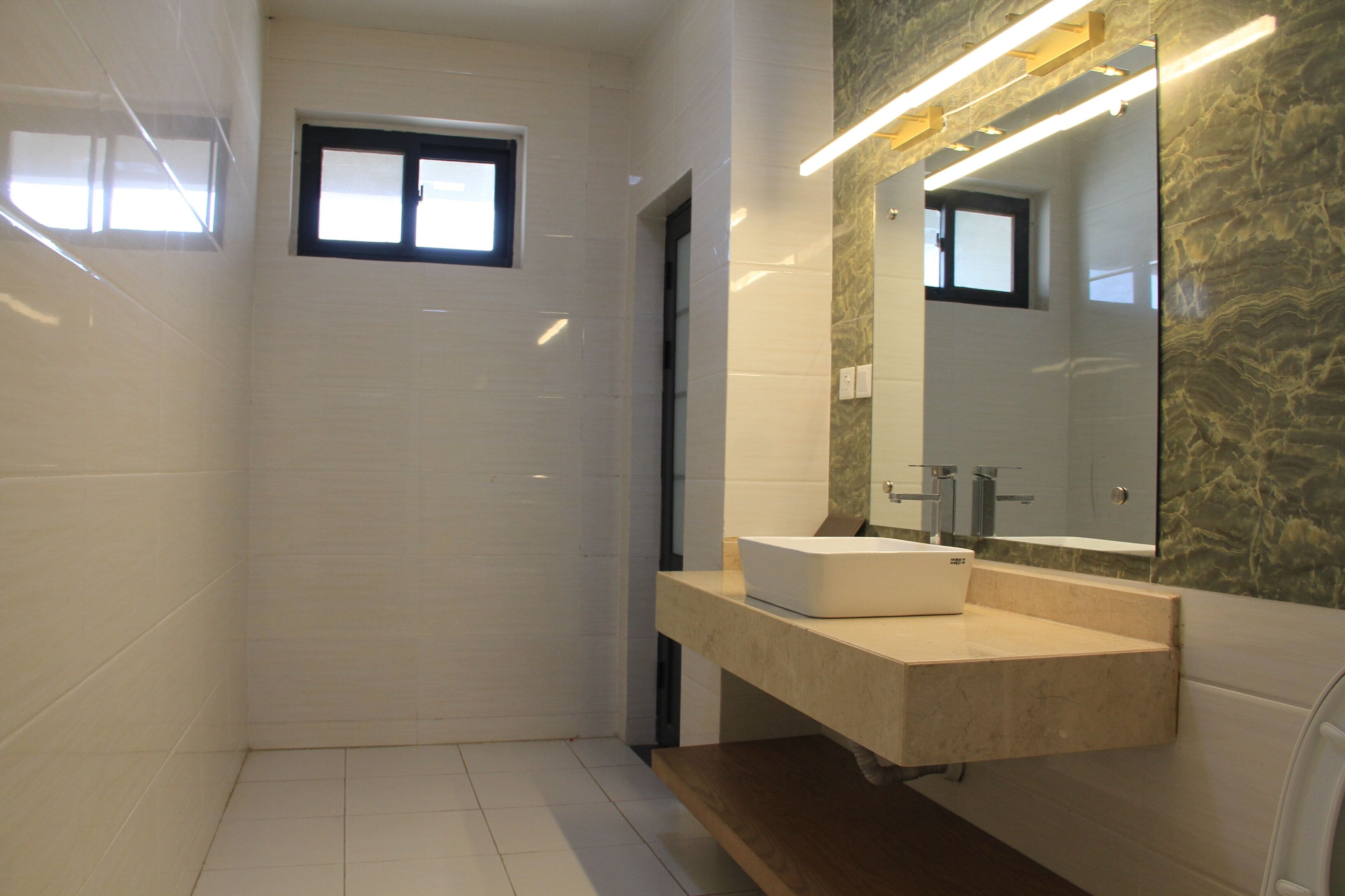 Un baño moderno con azulejos blancos, un espejo grande y un lavabo empotrado.