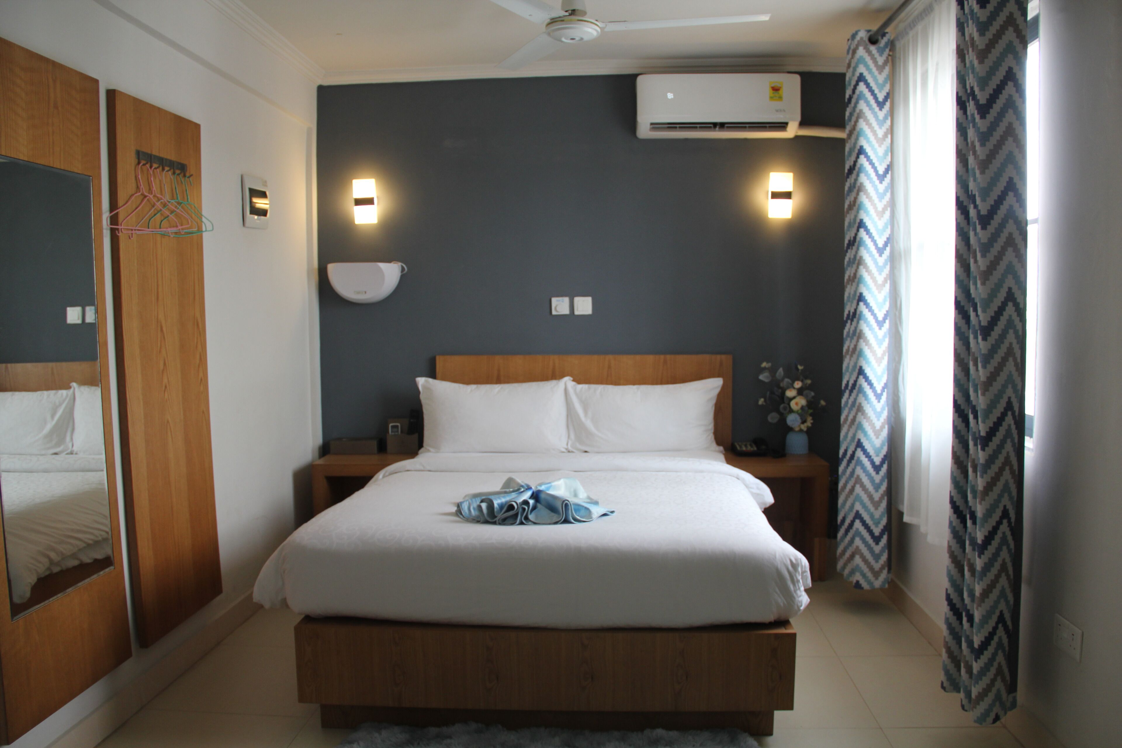 Una habitación de hotel con una cama grande, cabecera de madera, mesitas de noche, ventilador de techo y aire acondicionado.