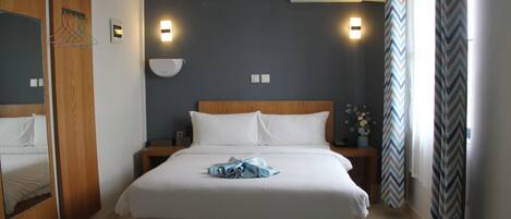 A hotel room with a large bed, wooden headboard, bedside tables, a ceiling fan, and an air conditioning unit.