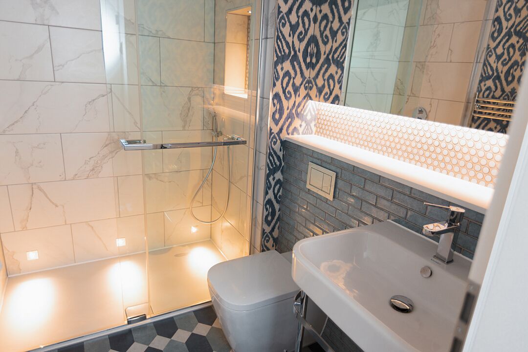 Een moderne badkamer met een douche met glazen wand, een wit wastafelmeubel en een decoratieve spatwand, en een kleine prullenbak.