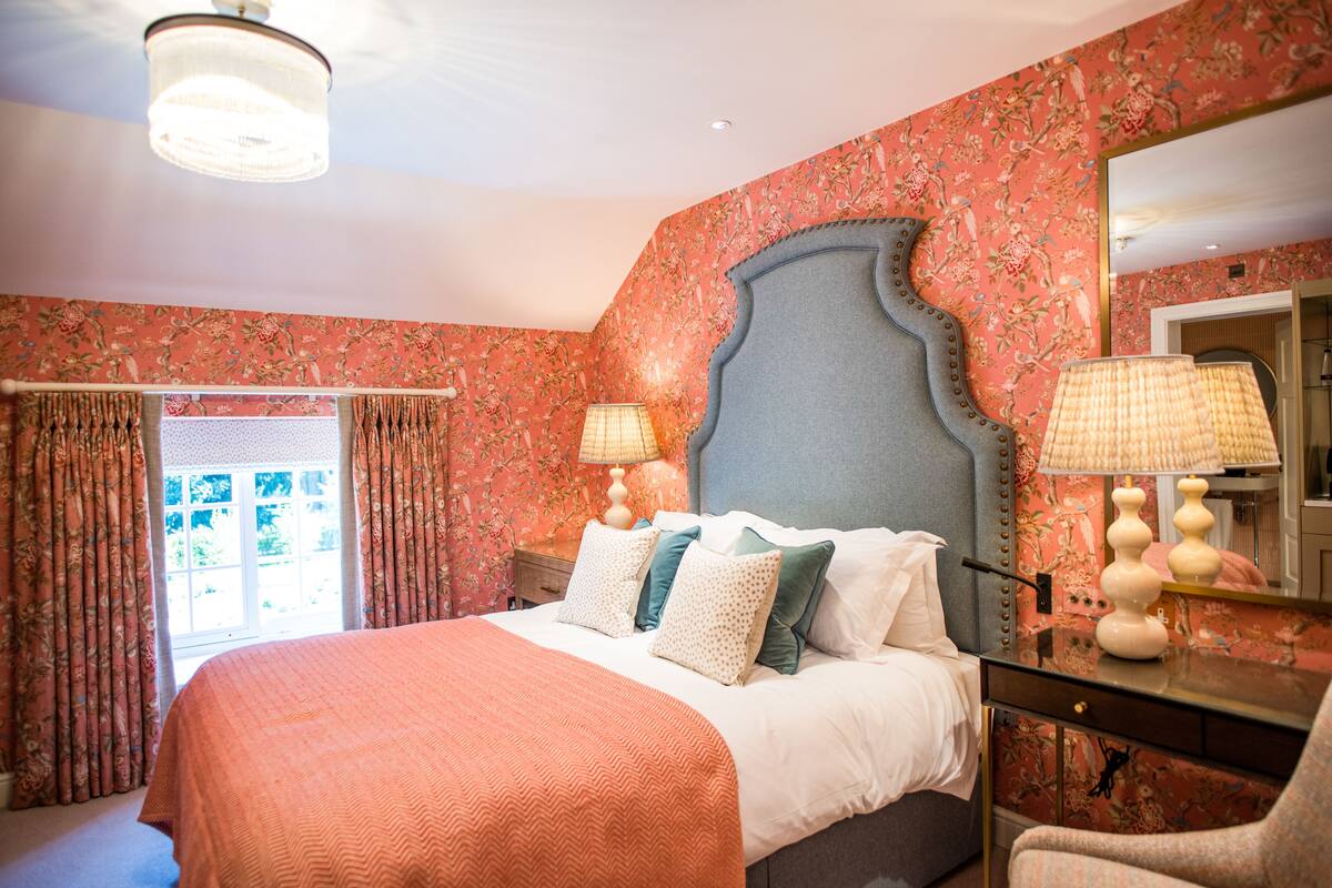 A bedroom with a bed, two bedside lamps, a dresser, a mirror, and floral wallpaper.