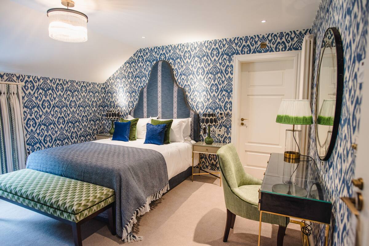 A bedroom with a bed, bedside table, chair, and a mirror.