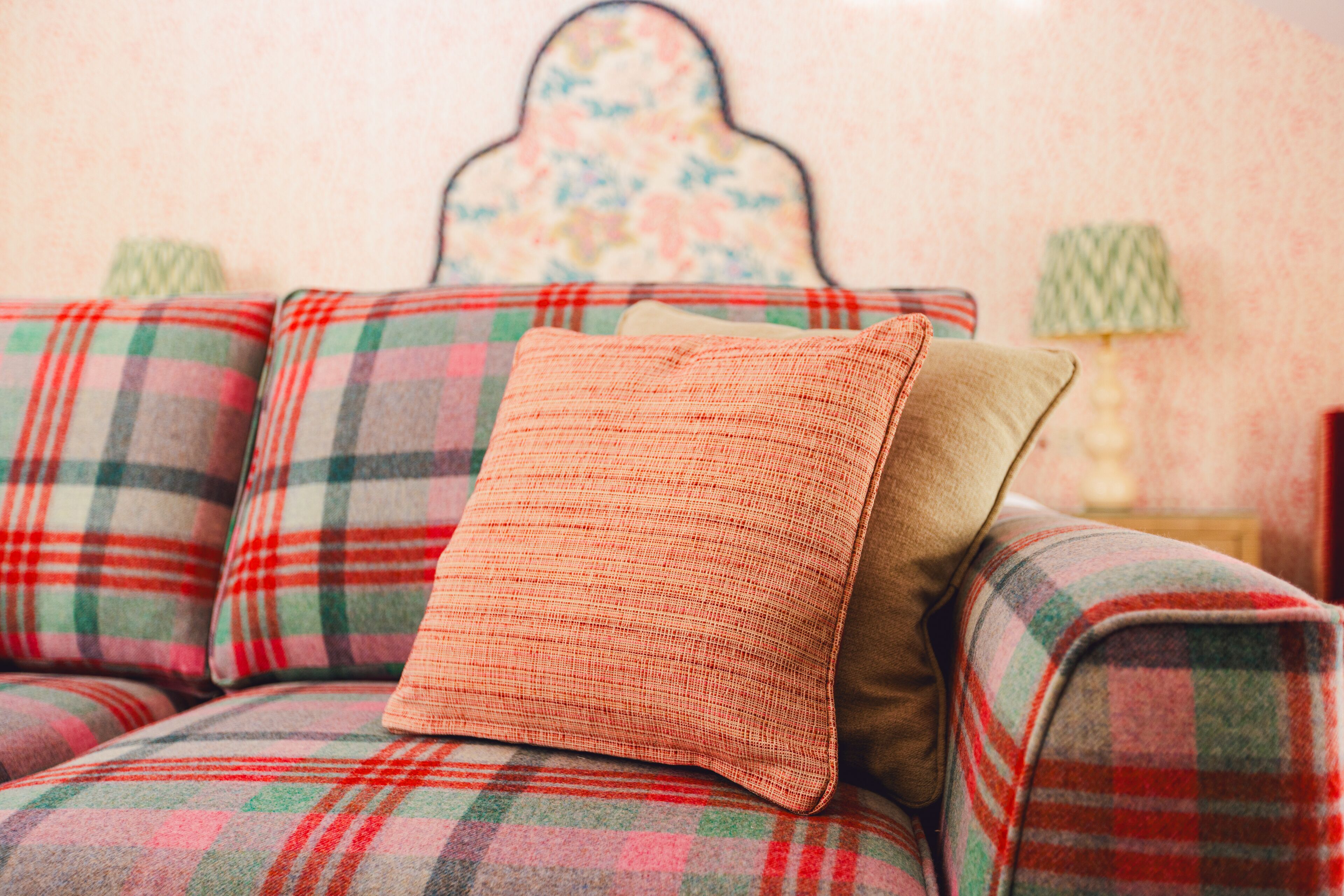 A plaid sofa with a single orange cushion.