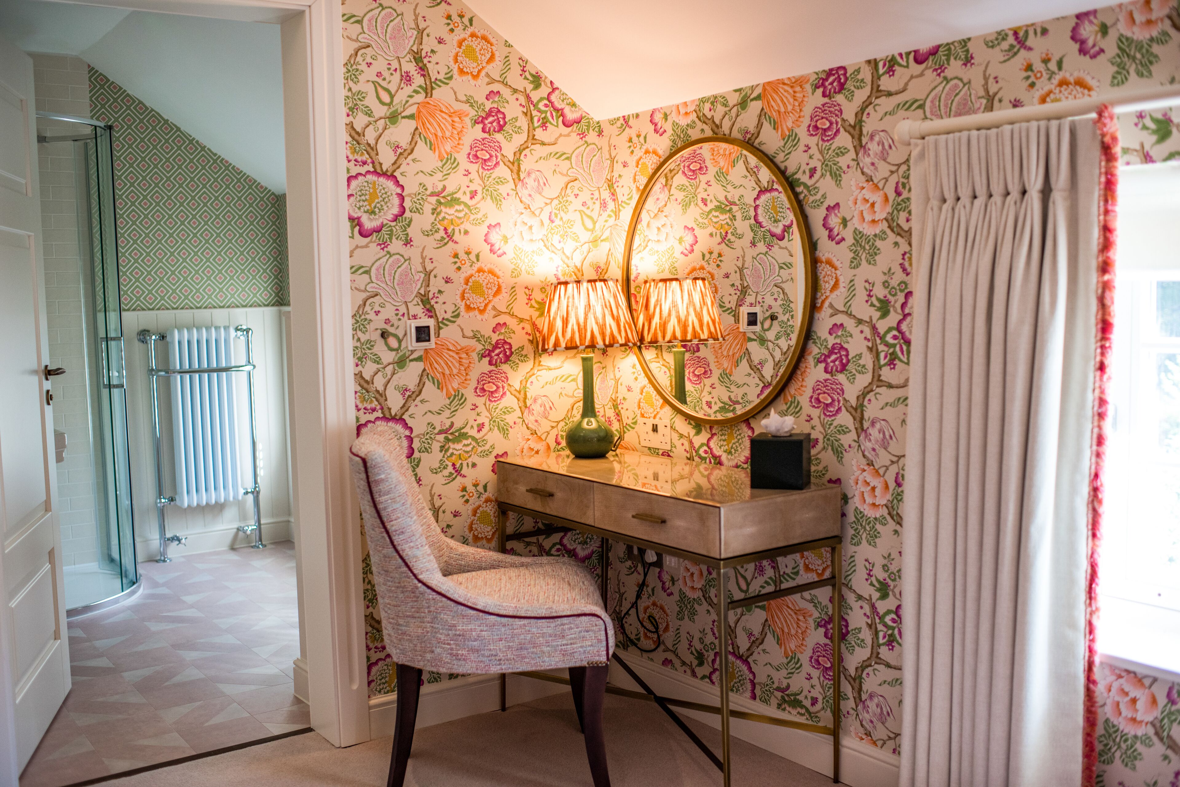 Un baño con ducha, tocador con espejo y papel tapiz con motivos florales.