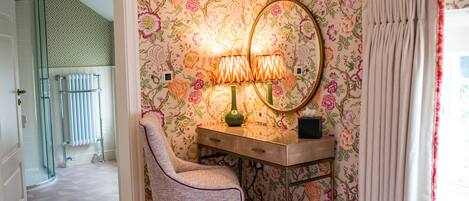 Un baño con ducha, tocador con espejo y papel tapiz con motivos florales.