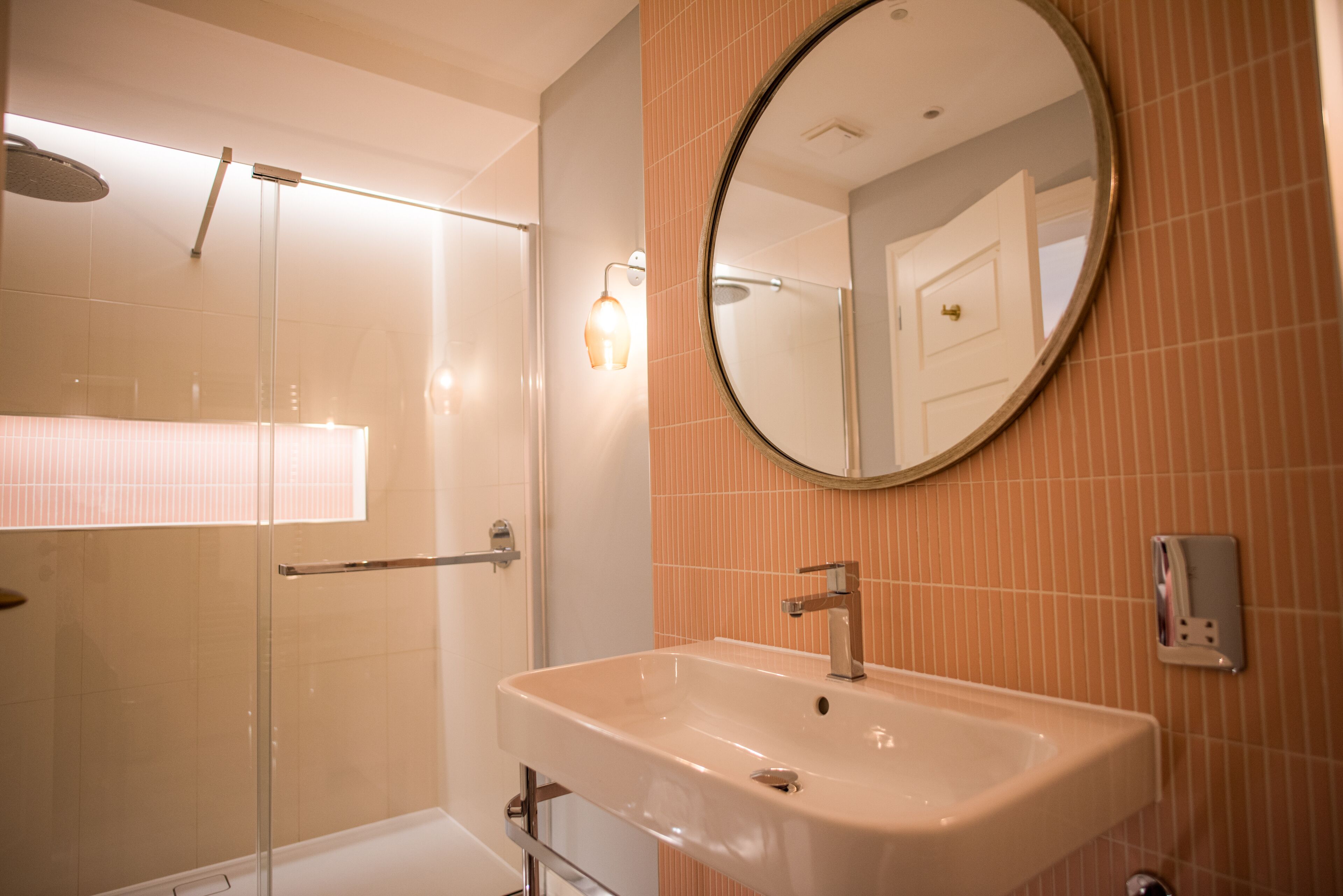A modern bathroom with a glass-enclosed shower, a sink with a mirror above it, and a light fixture on the wall.