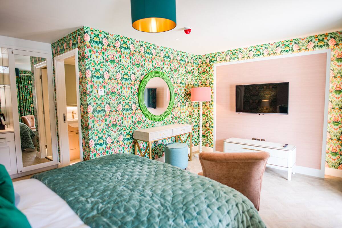 A bedroom with a bed, a dresser, a mirror, a television, and a door leading to another room.